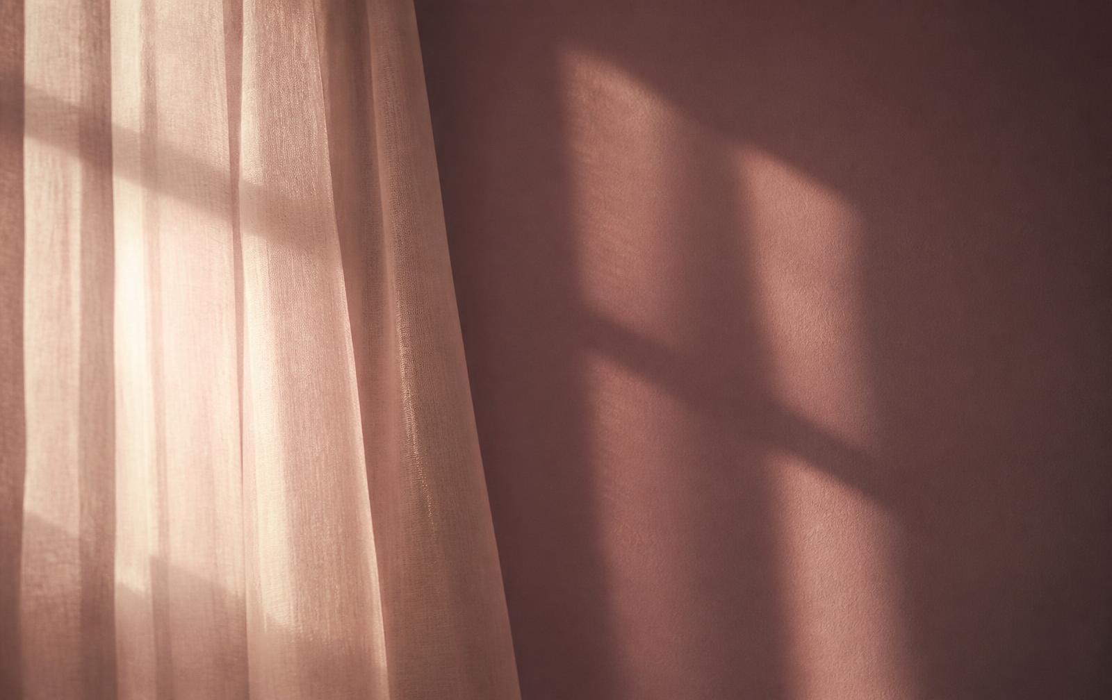 Sunlight through a sheer curtain against a soft plum wall